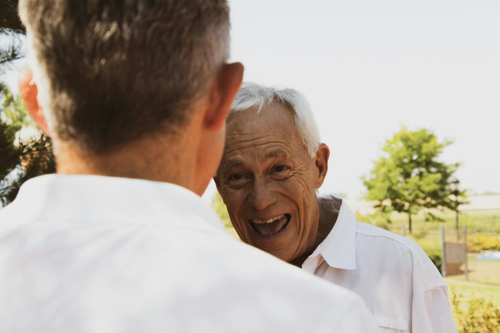 Smiling beautiful audiologist demonstrating proper fitting of a hearing aid device to a senior male customer during a consultation at an audiology center, enhancing communication and quality of life